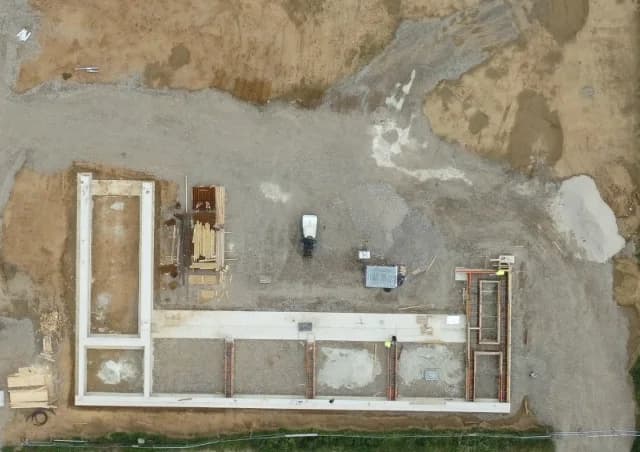 Luftbild des Baufelds: L-förmige Fundamentkontur des Neubaus