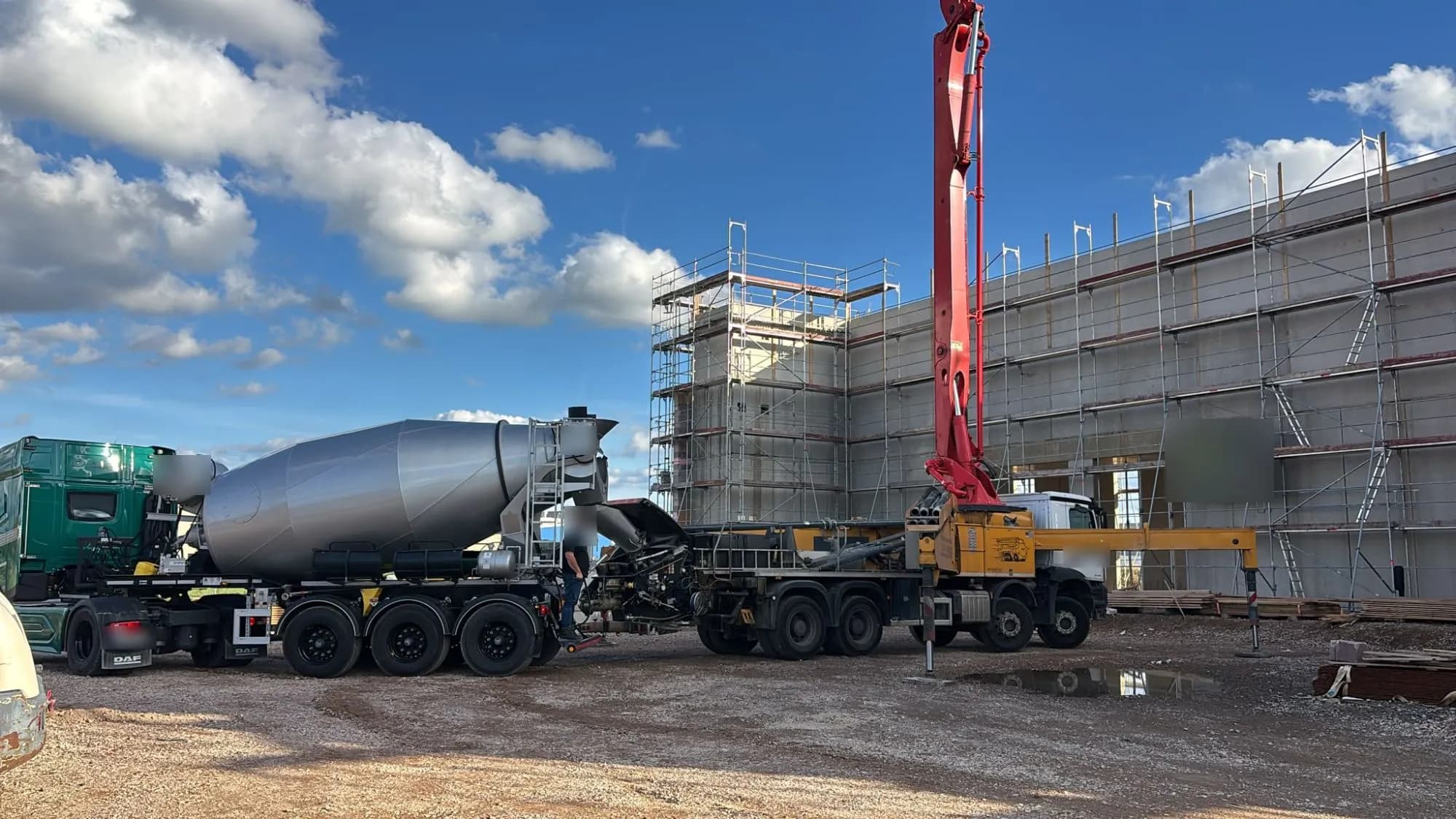 Fahrmischer übergibt Beton an die Betonpumpe vor der Hallenwand