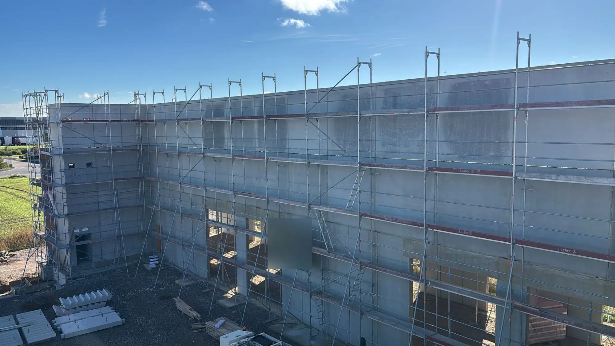 Eingerüstete Hallenfassade aus Betonfertigteilen, Tor- und Fensteröffnungen im Erdgeschoss