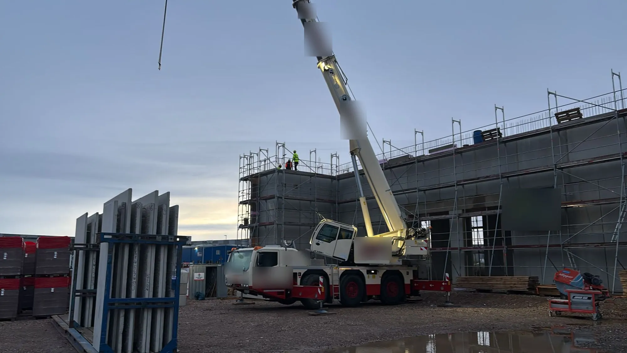 Mobilkran setzt Betonfertigteile auf den eingerüsteten Rohbau
