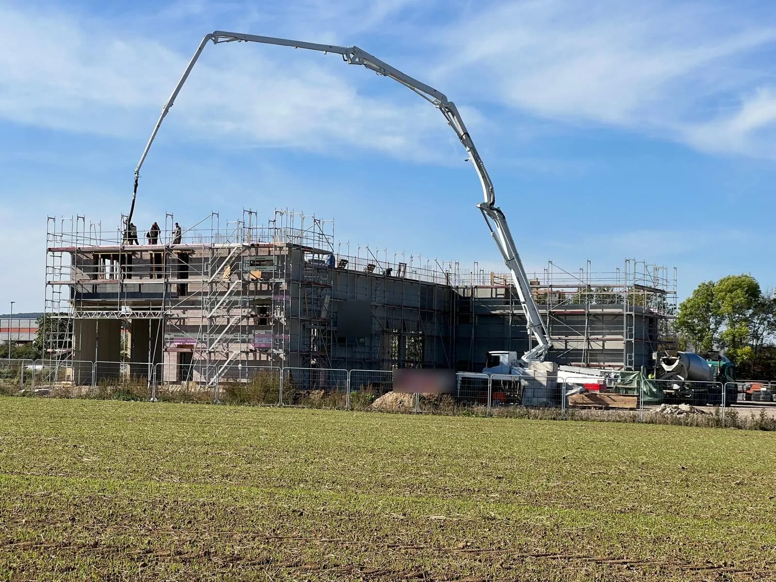 Rohbau von der Feldseite: Betonpumpe über dem eingerüsteten Bürotrakt, Halle dahinter