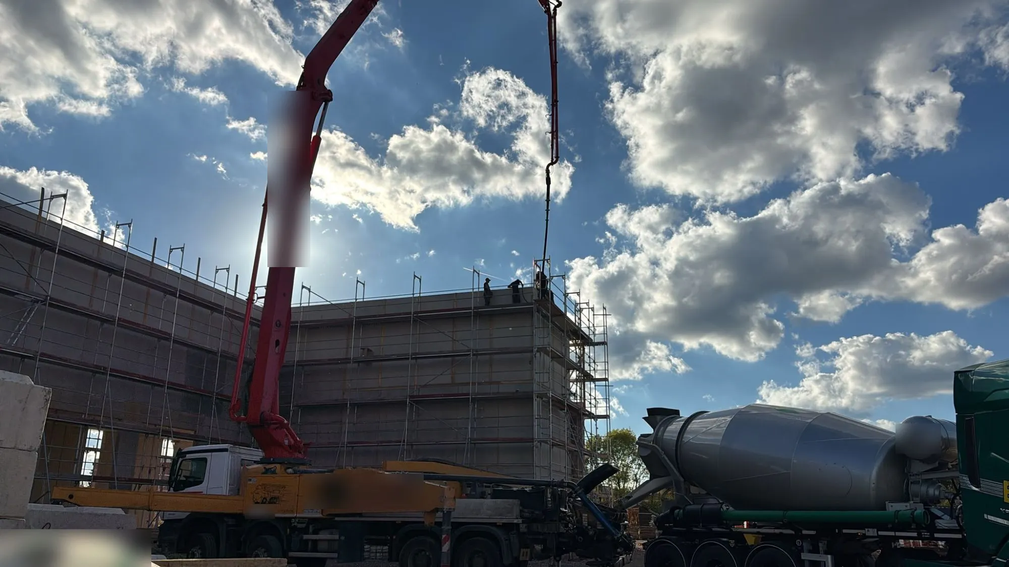 Betonpumpe fördert Beton auf das Dach des Rohbaus, Fahrmischer im Vordergrund